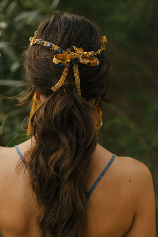 Coroa Lakkos com efeito de fita em latão com pedras azuis e flores em latão banhado a ouro fecho como um laço